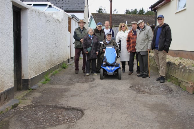 Whitehall residents inspect their potholed road (left to right) Bill Nicholls, Sheila Nicholls, Bob Thorne, Paul Stevens, Robbie Baker, Brian Tankhurst, Philip Sealey, and John Bowcock, with Ann Thorne in the mobility scooter.
