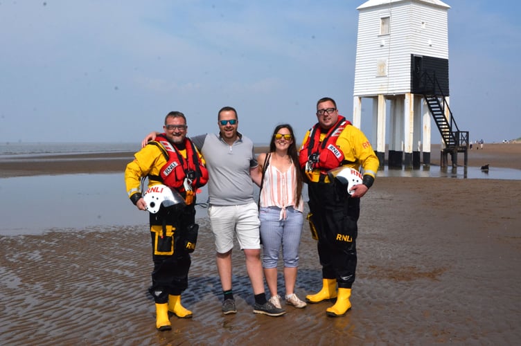 Lyndon and Kelly with lifeboat crew Daren and MarcPhoto released May 15 2024. RNLI volunteer surprises partner with unique proposal - with lifeboat crew holding up huge banner on the waves.Lyndon and Kelly were walking along Burnham-On-Sea beach on Sunday (12 May) - when a lifeboat appeared on the waves with RNLI crew holding a three metre banner stating: Marry me, Kelly?.After nearly 20 years together, Lyndon, the Burnham-on-Sea RNLI Deputy Press Officer, decided there was no better place to get down on one knee than on the coastline in front of RNLI's Lower Lighthouse.Lyndon, who had spent spent weeks planning the very special moment with the help of crew, said: "Thankfully she said yes!"