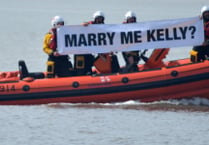 RNLI volunteer's surprise proposal with crew holding banner on waves