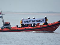 RNLI volunteer's surprise proposal with crew holding banner on waves