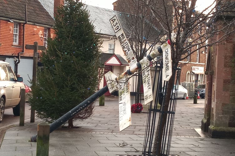 The damaged Nether Stowey fingerpost wit the village Christmas tree inn the background.