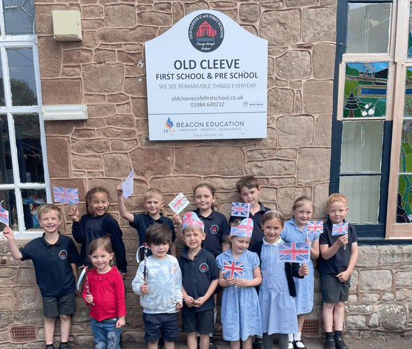Youngsters in Old Cleeve First School wave flags they made for the 80th anniversary of VE Day. PHOTO: Beacon Education.