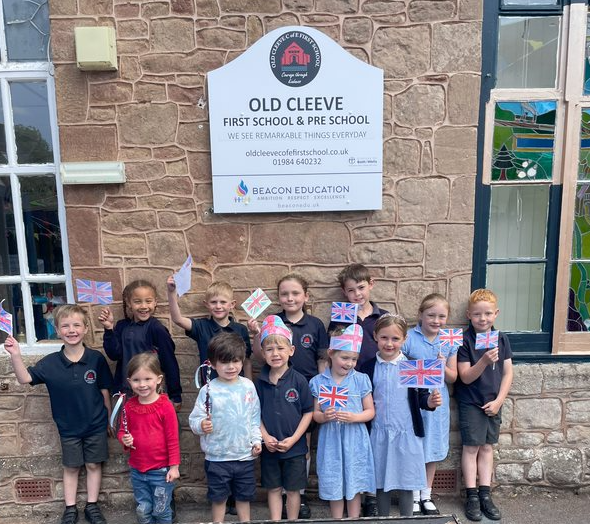 Youngsters in Old Cleeve First School wave flags they made for the 80th anniversary of VE Day. PHOTO: Beacon Education.
