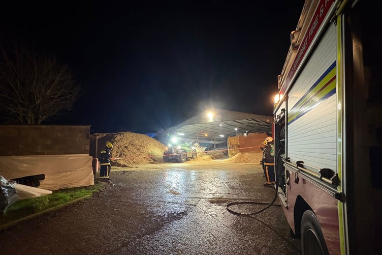 Firefighters watch on as a farmer uses a telehandler to drag straw from a barn which caught alight.