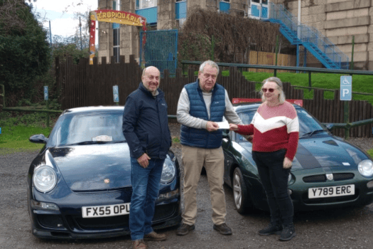 Minehead Motor Club members Clive Rayson and Denise Woodward hand over a cheque to Chris Moiser (centre) from Tropiquaria Zoo.